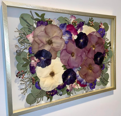 Framed artwork of pressed flowers with a gold frame on a white wall